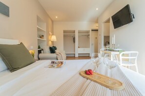 A hotel room with a bed, a dining table with wine glasses and strawberries, a TV mounted on the wall, and a closet. - MT Studio 1 by Rent All Como (Como)
