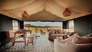 A tented room with a wooden table, cushioned seating, and a view of the landscape. - Safari Tent in Stiffkey Valley With Fire Pit (Walsingham)