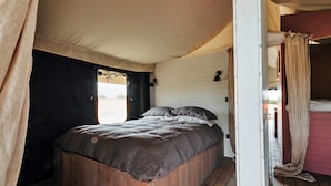A single bed with a wooden frame and a dark-colored bedspread in a room with white walls and a wooden floor. - Safari Tent in Stiffkey Valley With Fire Pit (Walsingham)