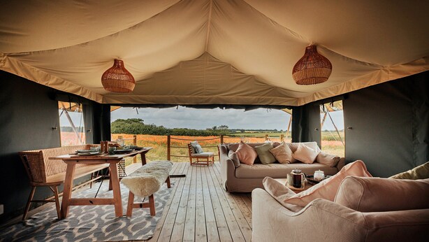 A tented room with a wooden deck, a sofa, a table, and a chair. - Safari Tent in Stiffkey Valley With Fire Pit (Walsingham)