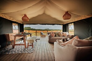 A tented room with a wooden deck, a sofa, a table, and a chair. - Safari Tent in Stiffkey Valley With Fire Pit (Walsingham)