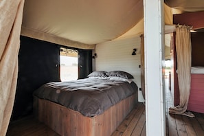 A wooden bed in a tent-like room with a white wall and a curtain. - Safari Tent in Stiffkey Valley With Fire Pit (Walsingham)