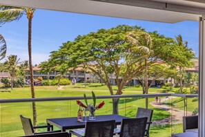 A balcony with a table and chairs, overlooking a well-maintained lawn and trees.