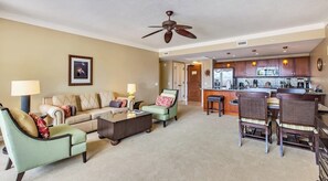 A living room with a sofa, chairs, a coffee table, and a kitchen area with a bar.