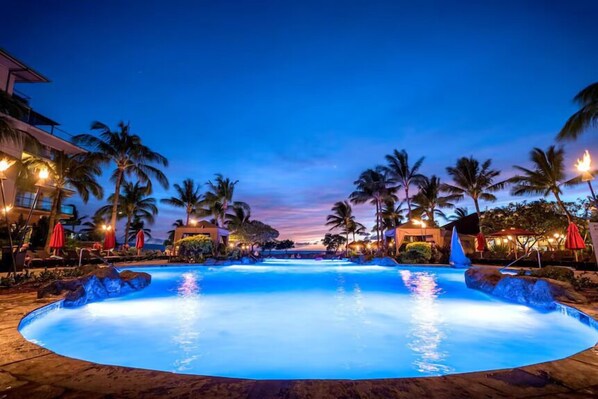 A large outdoor swimming pool surrounded by palm trees and hotel buildings.