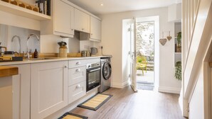 A modern kitchen with white cabinets, a built-in oven, and a washing machine. - Eldred Cottage, Middleham (Middleham, North Yorkshire)