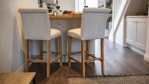 A kitchen with two bar stools, wooden flooring, and a view of the dining area. - Eldred Cottage, Middleham (Middleham, North Yorkshire)