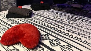 Une chambre d’hôtel moderne avec un lit, un coussin rouge, un tapis à motifs et un plafond éclairé en bleu.