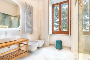 Een moderne badkamer met een groot wastafel, een toilet met watervloed en een raam met uitzicht op bomen.