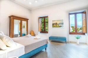 Een slaapkamer met een bed, een bankje, een spiegel, een schilderij en een raam met uitzicht.