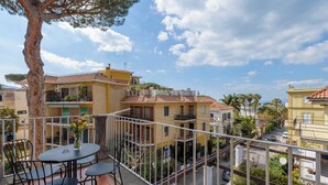 A balcony with a table and chairs, overlooking a residential area with buildings and a tree. - Maramia Luxury Apartment (Sant'Agnello)