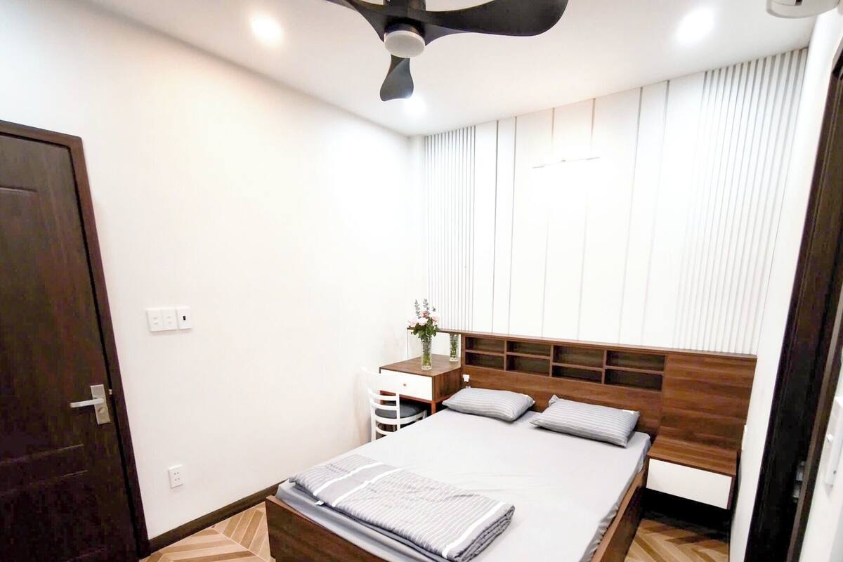 Ein Schlafzimmer mit einem Bett, einem Nachttisch, einem Deckenventilator und einer Tür.