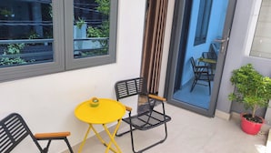 Ein kleiner Außenbereich mit einem gelben Tisch und schwarzen Stühlen, einem Blumentopf und einer Schiebetür, die auf einen Balkon führt.