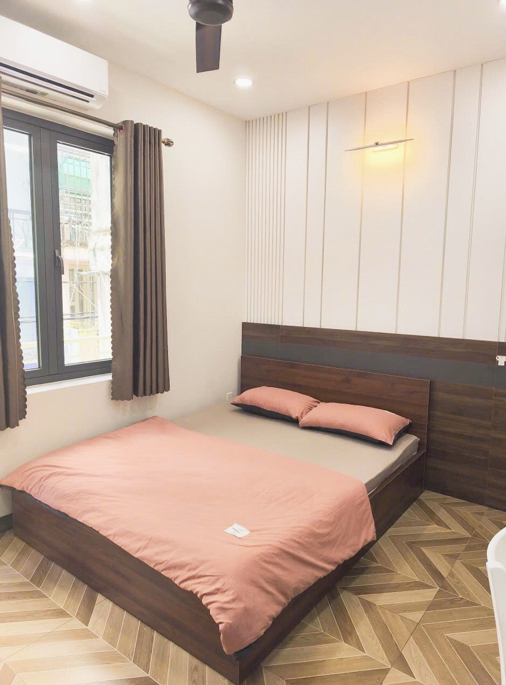 Une chambre à coucher avec un lit, une fenêtre avec des rideaux, un climatiseur et un luminaire fixé au mur.