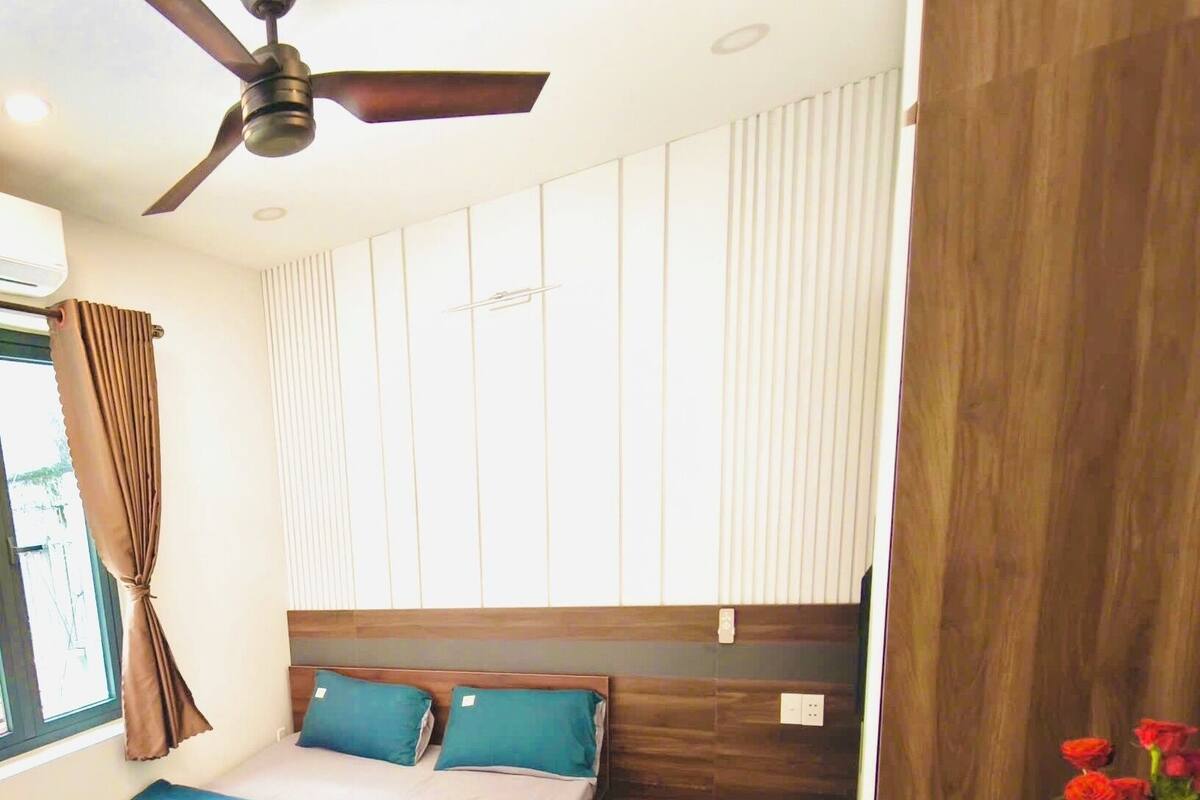 Ein Schlafzimmer mit einem Bett, einem Holz-Kopfstück, einem Fischgrätenparkettboden, einem Deckenventilator und einem Fenster mit Vorhängen.