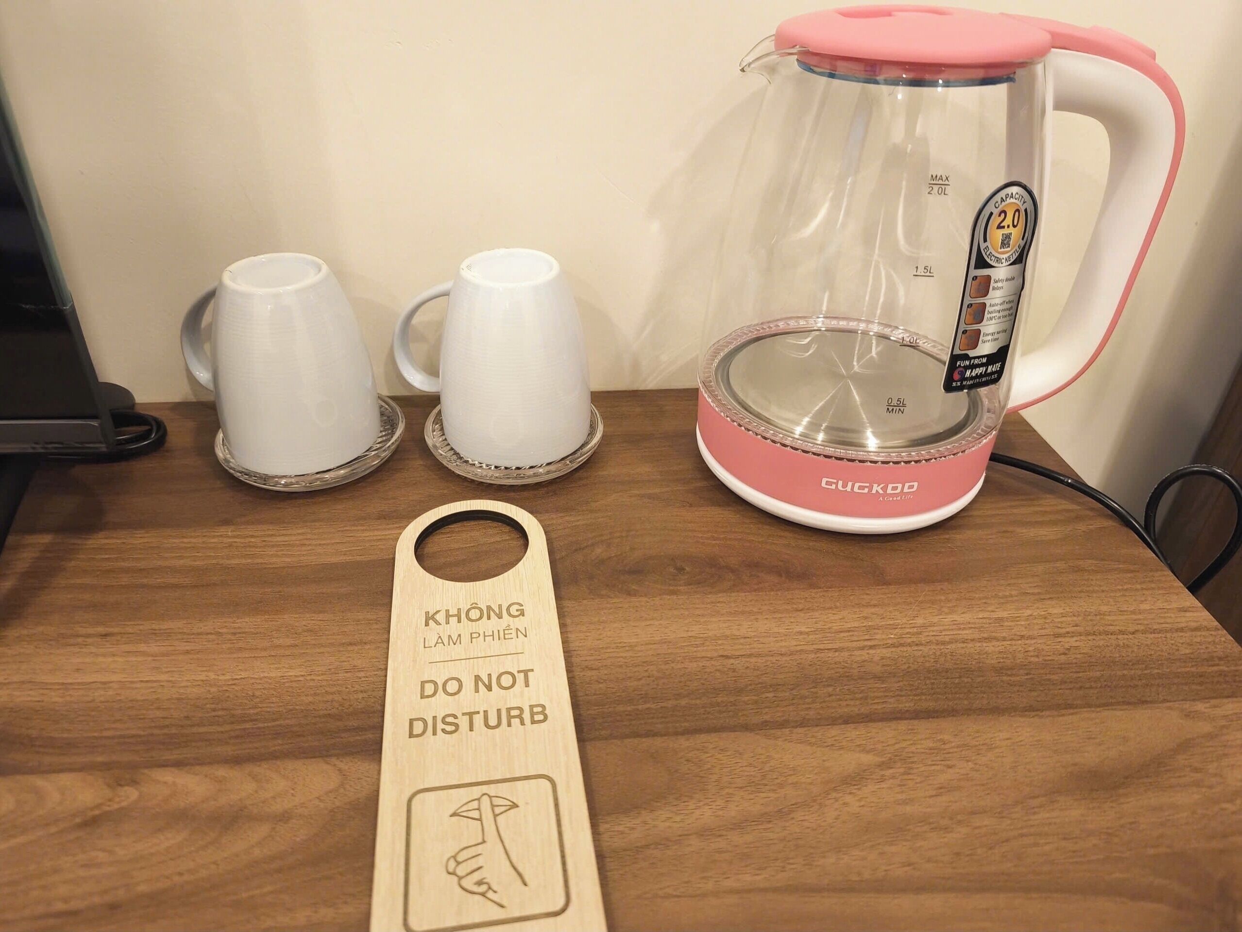 A coffee maker, two white cups, and a wooden sign on a wooden table.
