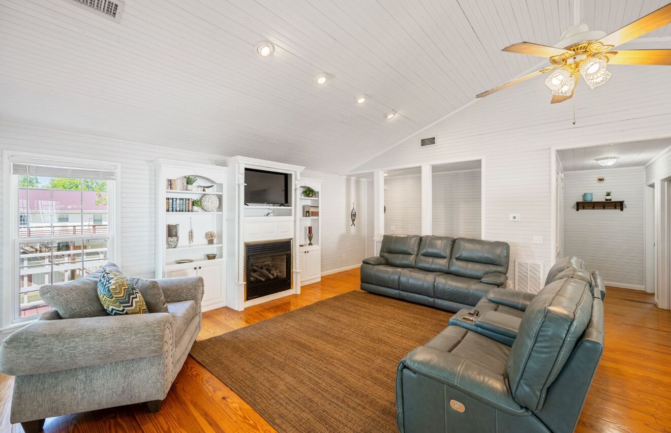 A spacious living room with a fireplace, a ceiling fan, and a large window.