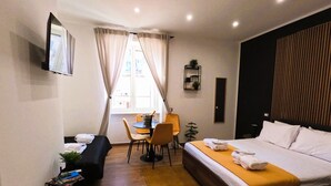 Ett hotellrum med en säng, ett skrivbord, en stol och ett litet bord med en växt.