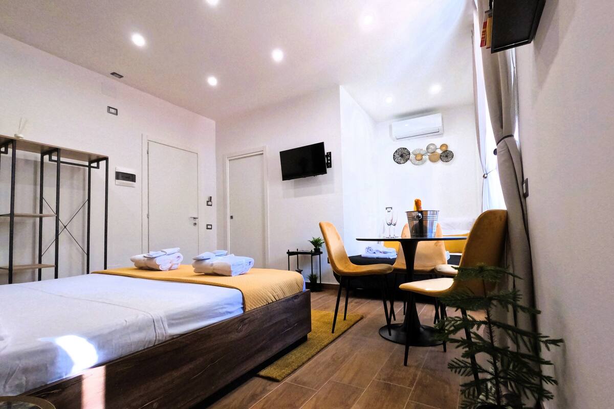 A hotel room with a bed, a desk, a chair, a television, and a potted plant.