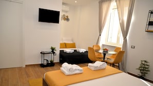 Ett hotellrum med en säng, ett skrivbord, en stol, en tv och ett fönster med gardiner.