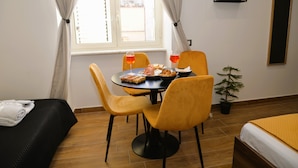 Ett hotellrum med en säng, ett matbord med stolar, en liten krukväxt och ett fönster med gardiner.