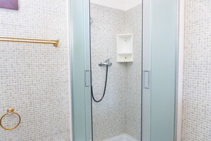 Una ducha con puerta de vidrio, un lavamanos blanco y un perchero para toallas.