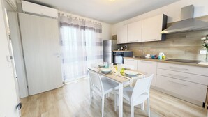 Une cuisine moderne avec des armoires blanches, une hotte en acier inoxydable et un coin repas avec une table dressée pour quatre personnes.