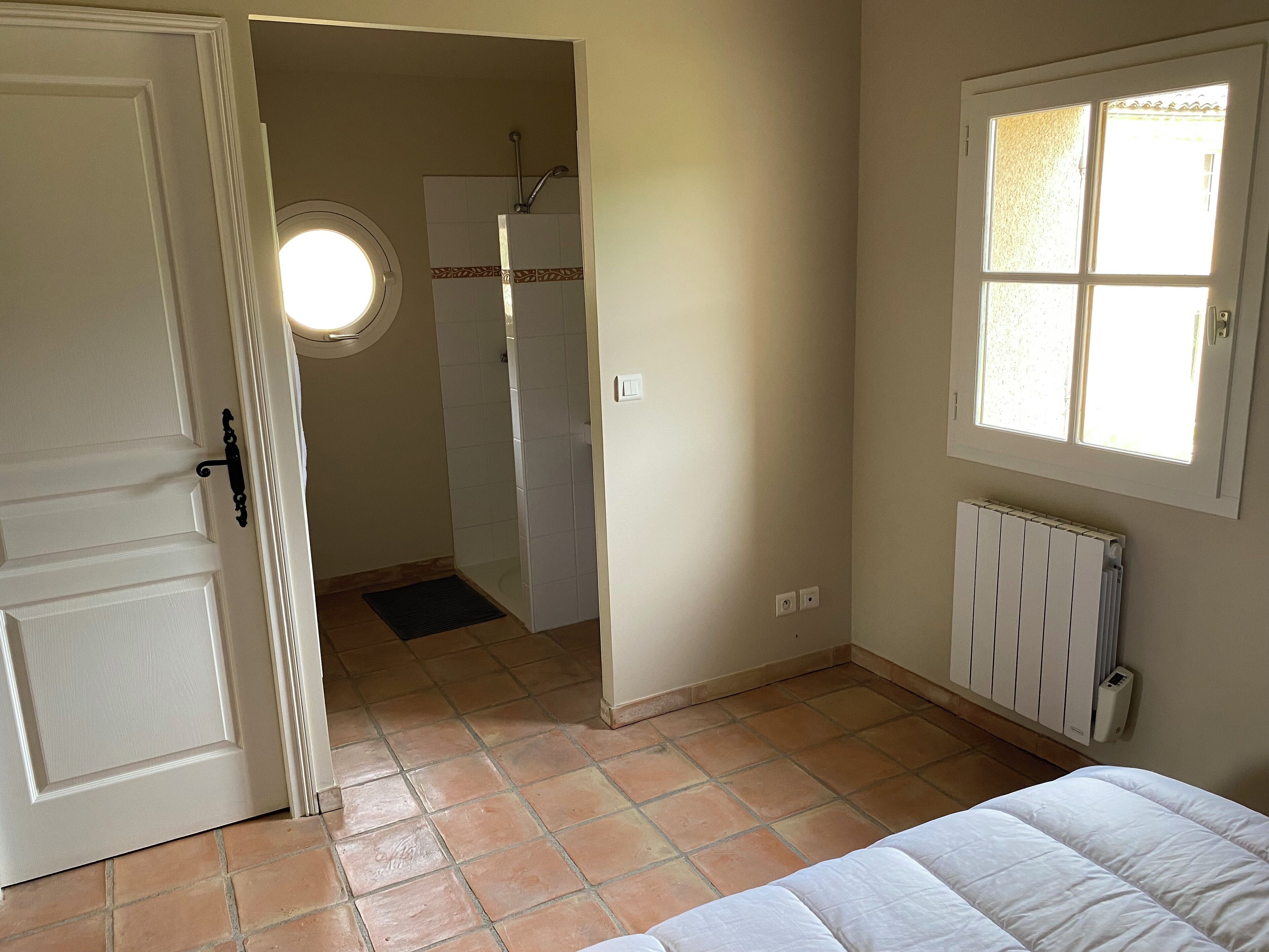 A room with a bed, a radiator, a window, and a door leading to a bathroom.