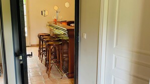 Un pasillo que conduce a un comedor con una mesa y sillas de madera, suelo de baldosas y una puerta blanca.