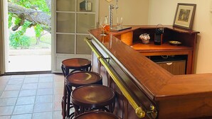 Zona de bar con mostrador de madera, taburetes y vistas a la vegetación a través de un ventanal.