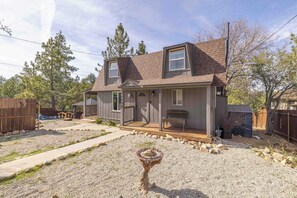 A two-story house with a front porch, a small deck, and a gravel driveway.