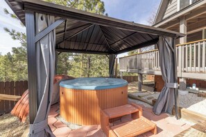 A hot tub under a covered patio with wooden steps and a wooden deck in the background.