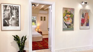 Een hal met een bed, een rode potplant en kunstwerken aan de muur.