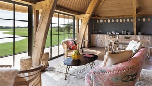A spacious room with large windows, a wooden ceiling, a dining area, and a cozy seating area with a sofa and chairs.