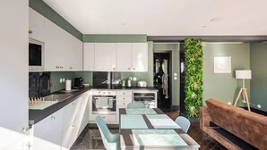 A modern kitchen with white cabinets, a black countertop, and a dining area with a table and chairs. - City Garden - A green setting in the heart of Dijon (3 stars) (Dijon)