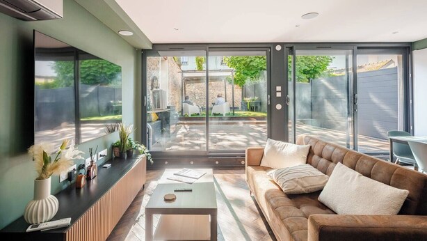 A modern living room with a sofa, coffee table, and a glass door leading to an outdoor patio. - City Garden - A green setting in the heart of Dijon (3 stars) (Dijon)