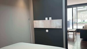 A modern bedroom with a skylight, a bed with a quilted cover, a built-in shelf with two small items, and a view of an outdoor patio area. - City Garden - A green setting in the heart of Dijon (3 stars) (Dijon)