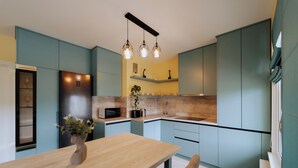 A modern kitchen with teal cabinetry, a wooden dining table, and pendant lighting. - Full Amenities, Modern 1BR • near Medpark Riscani (Chișinău)