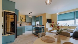 A modern kitchen with teal cabinetry, a dining area with a round table, and a sofa. - Full Amenities, Modern 1BR • near Medpark Riscani (Chișinău)
