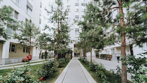 A pathway flanked by trees and bushes, leading to a building with multiple windows and balconies. - Full Amenities, Modern 1BR • near Medpark Riscani (Chișinău)