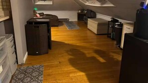 A compact, well-lit attic room with a sloped ceiling, a small sofa, a desk with a computer, and a television.