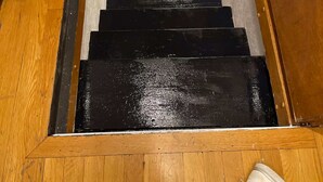 A wooden staircase with black steps leading to a landing.