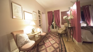 A cozy room with a patterned rug, a chair, a small table with a lamp, and a bed with curtains. - Porta Palace Apartments (Turin)