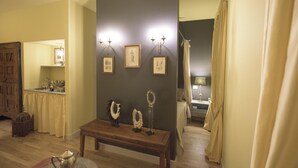 Ein Zimmer mit einer Holzbank, gerahmten Bildern an der Wand, einem kleinen Tisch mit Teekanne und einem Bett mit Vorhang.