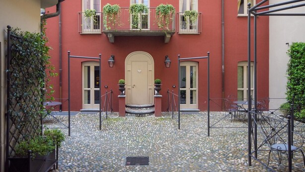 Ein Innenhof mit einem roten Gebäude, einer beigen Tür und einem kleinen Gartenbereich mit Blumentöpfen.