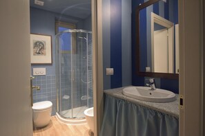 A bathroom with a glass-enclosed shower, a sink with a mirror, and a toilet. - Porta Palace Apartments (Turin)