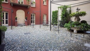 Ein Innenhof mit Kopfsteinpflaster, ein rotes Gebäude mit einer weißen Tür und ein kleiner Tisch mit Stühlen.