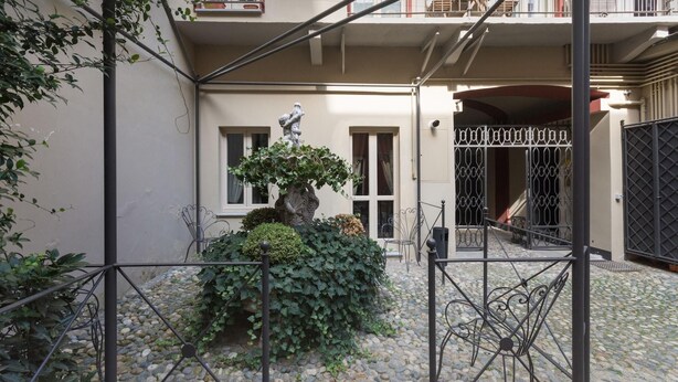 A courtyard with a stone floor, a metal gate, and a statue. - Porta Palace Apartments (Turin)