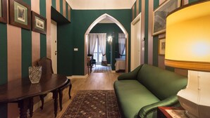 A room with a green sofa, a wooden table, and a chandelier. There is a door leading to another room. - Porta Palace Apartments (Turin)