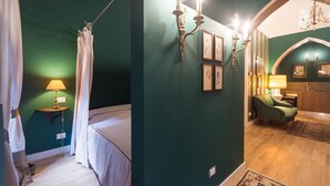 A bedroom with a bed, a nightstand, a lamp, a green armchair, and a chandelier. - Porta Palace Apartments (Turin)